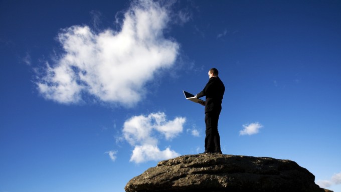 Man with laptop on top of rock with cloud in front of him.