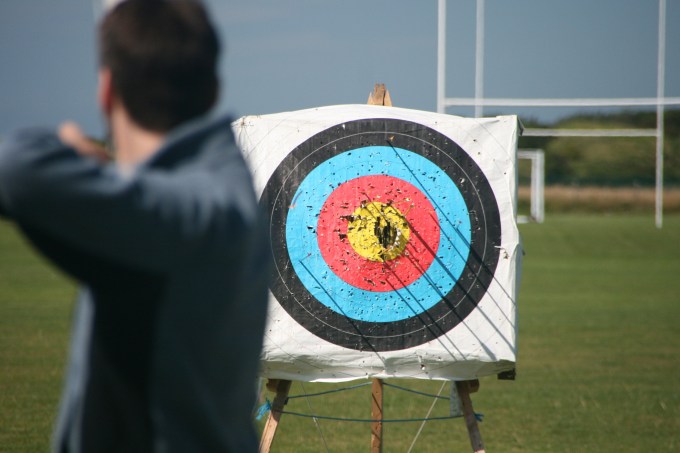 Man aiming bow and arrow at warn target.