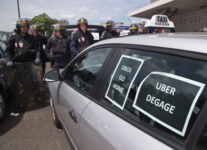 Riot police officers stand next to a cab with posters which reads, "Uber go home" and "Uber get out out," during a taxi drivers demonstration in Paris, France, Thursday, June 25, 2015. French taxis are on strike around the country, snarling traffic in major cities and slowing access to Paris' Charles de Gaulle airport after weeks of rising and sometimes violent tensions over Uber. (AP Photo/Michel Euler)