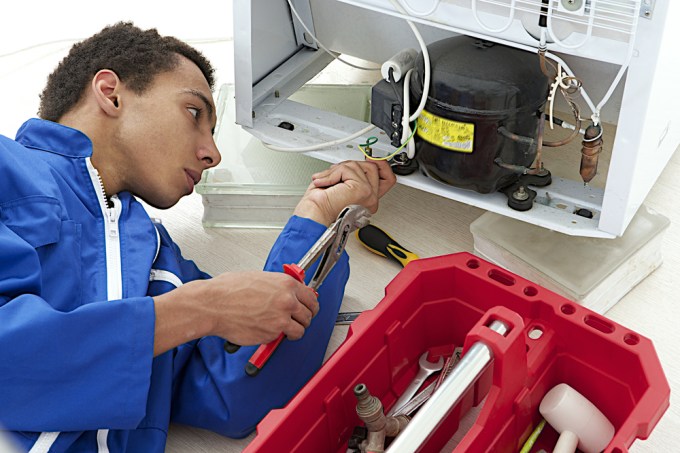 Young repair man fixing refrigerator.