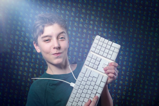 smiling teenage boy with computer keyboard and letters salad as background