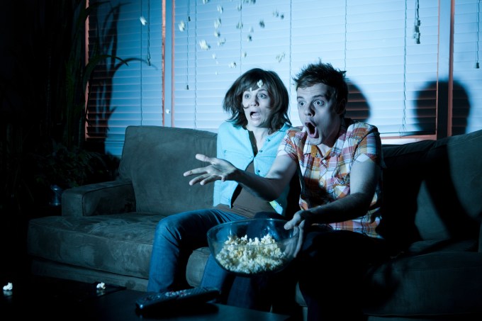 Young couple watching tv, man throwing popcorn