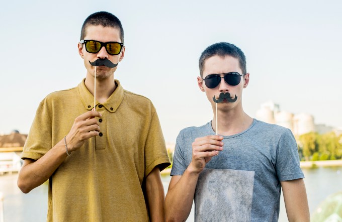 Caucasian men playing with fake mustaches in city