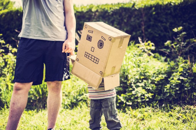 Little boy holding his daddys hand, wearing box over his head with robots face drawn on it.