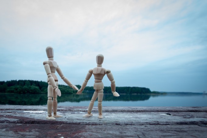 Two wooden figures holding hands in front of a lake.