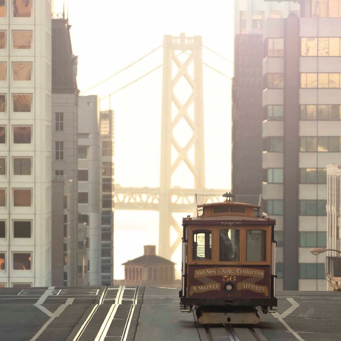 The Van Ness cable car as it reaches the top of Nob Hill in San Francisco on California Street with a view of the Bay Bridge in the background.