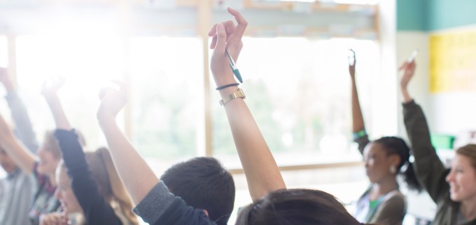 Teenage students with arms raised in classroom