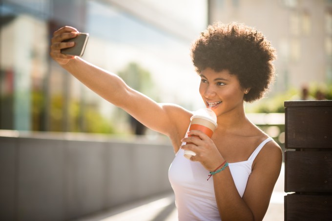 Pretty teen girl taking selfie while drinking takeaway coffee