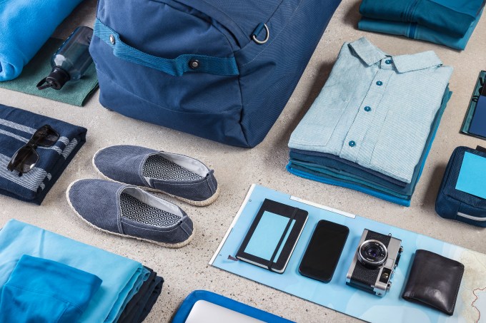 Overhead view of travel packing with blue shirt, retro camera, training shoes, smartphone and notebook